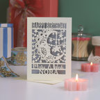 Laser-cut birthday card with decorative elements on a table with candles and gifts.