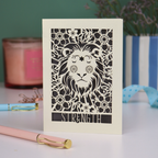 A laser cut greetings card based on the Strength tarot card, with cut out lion and floral design and the word "Strength" 