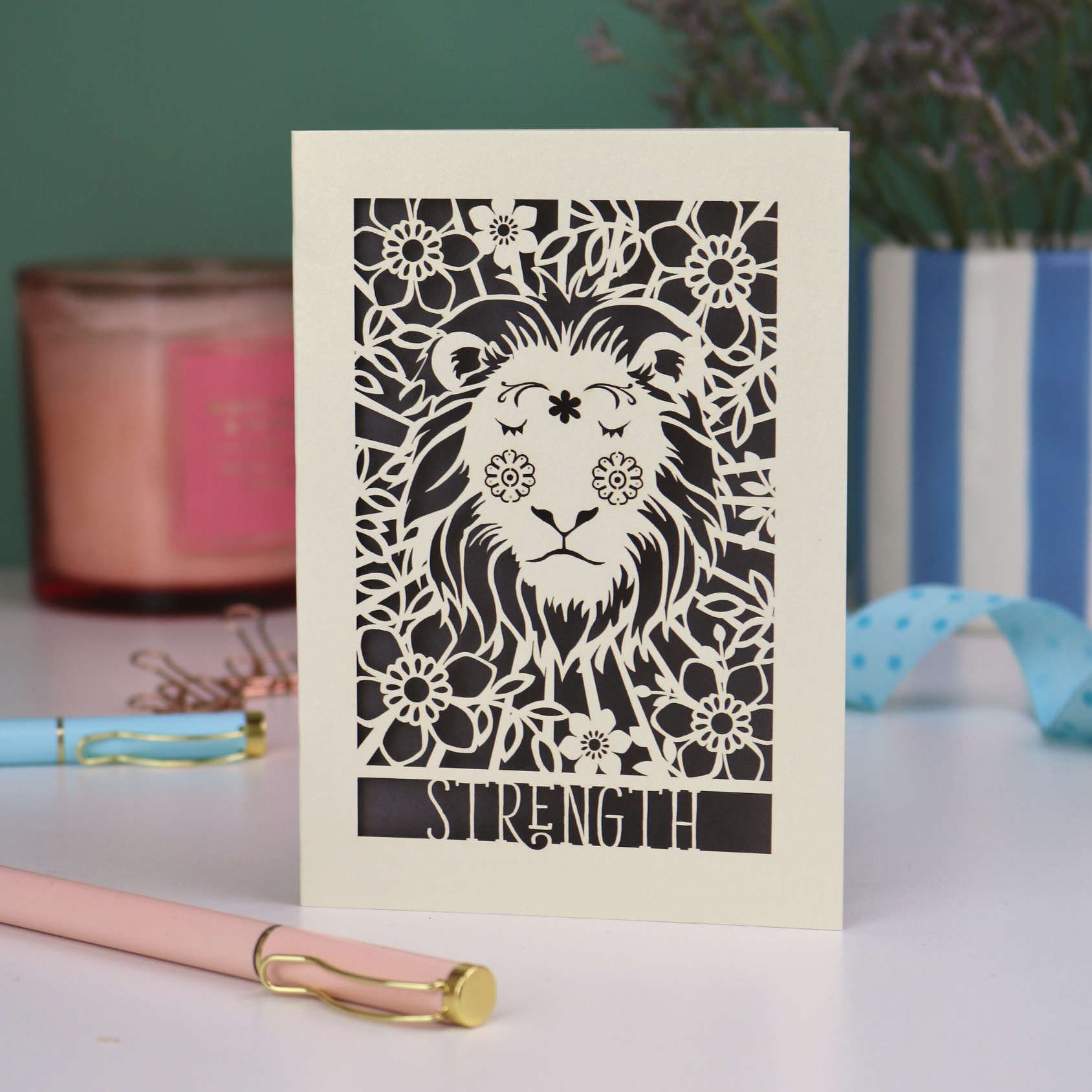 A laser cut greetings card based on the Strength tarot card, with cut out lion and floral design and the word "Strength" 