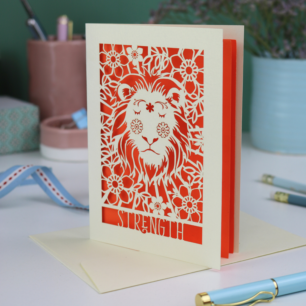 Decorative card with a lion design and 'Strength' text on a desk with stationery items.