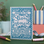 A wite card with blue printed design and text that says "Here's to Strong women, may we know them, may we be them, may we raise them"