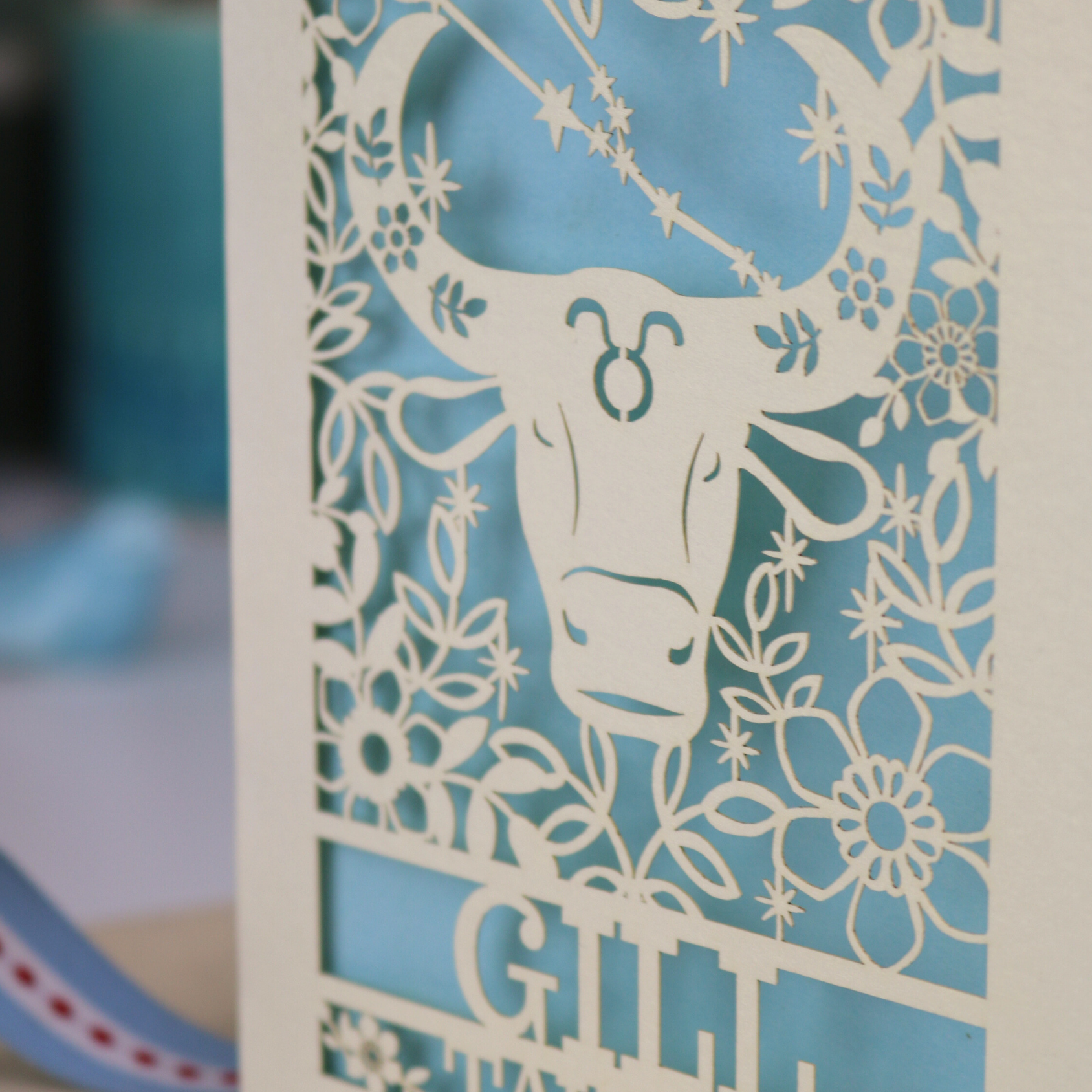 Personalised laser cut Birthday card with zodiac design featuring a bull on a pink background, with a pen and decorative ribbon in the foreground.