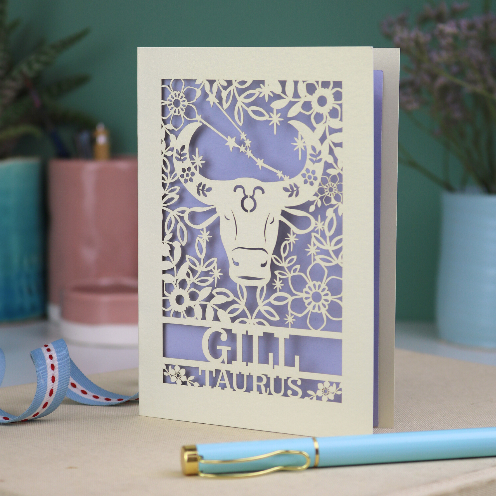 Personalised laser cut Birthday card with zodiac design featuring a bull on a pink background, with a pen and decorative ribbon in the foreground.