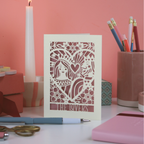 Decorative Valentine's card with intricate cut-out design on a desk with stationery items.