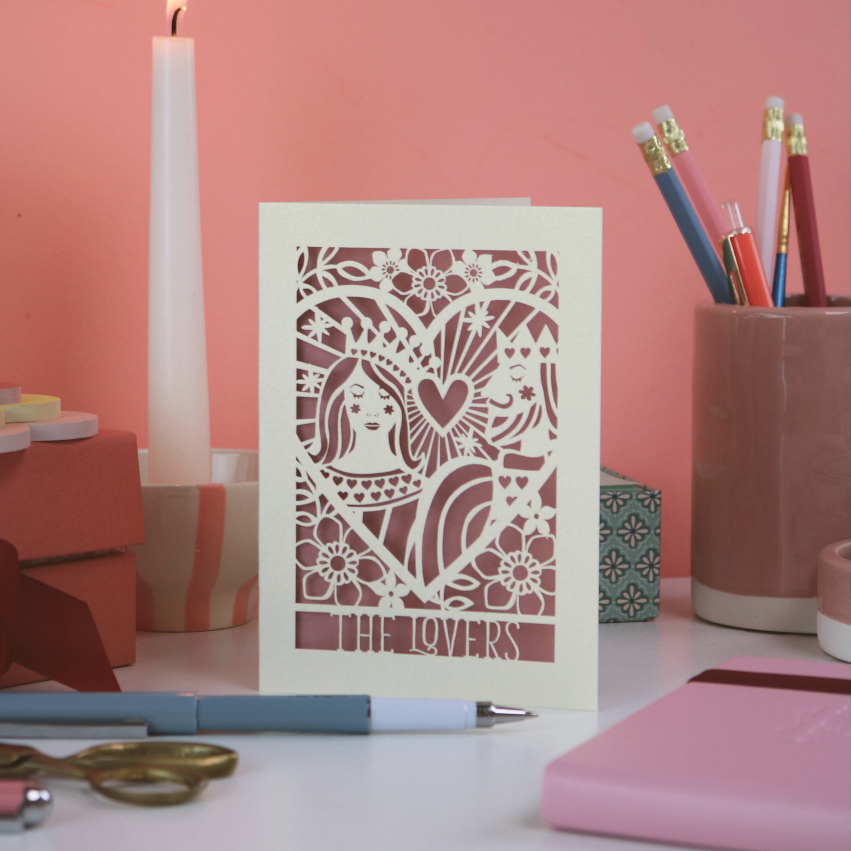 Decorative Valentine's card with intricate cut-out design on a desk with stationery items.