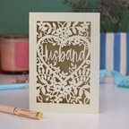 A laser cut husband valentines card with floral design on a green background