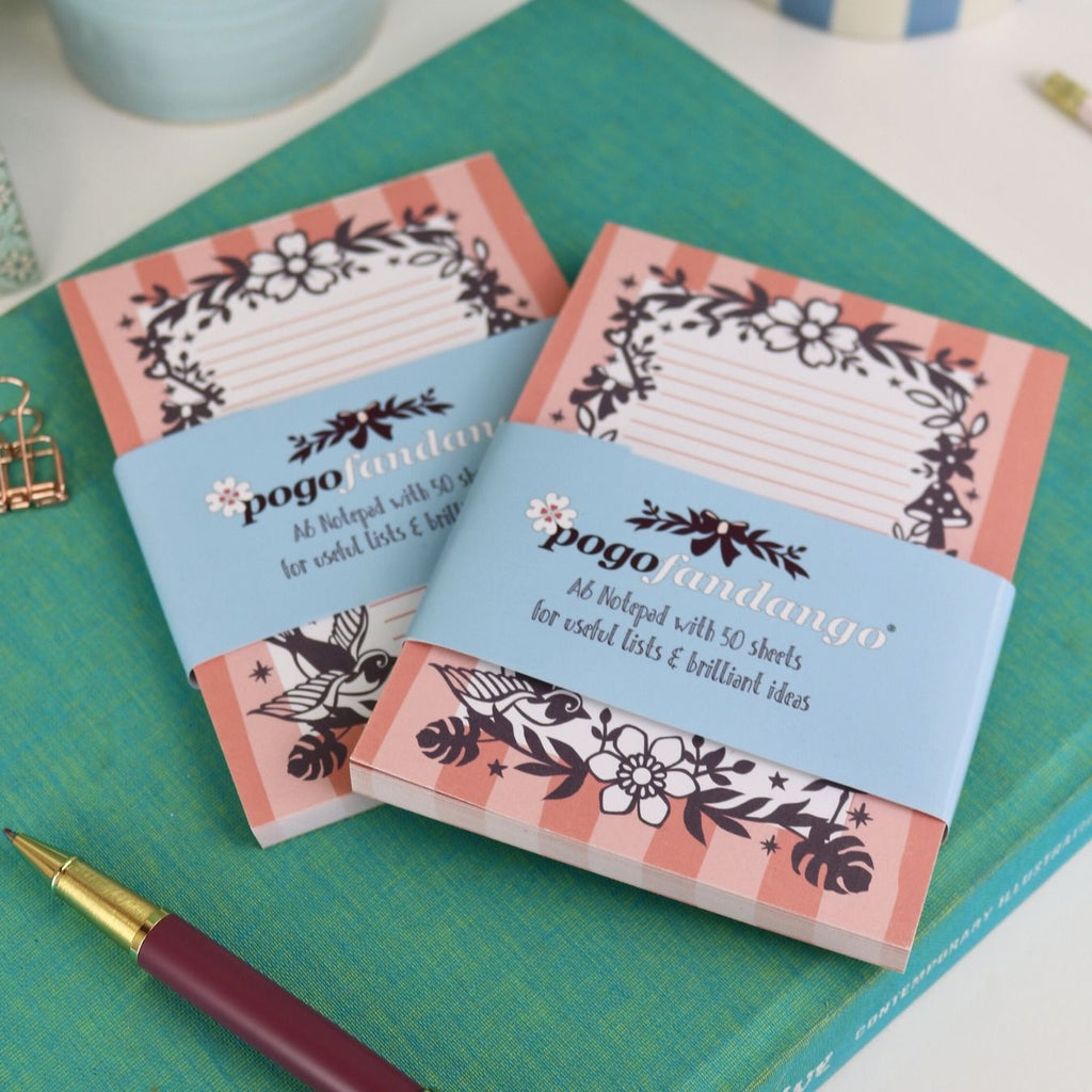 Two floral notepads with a pen on a green surface