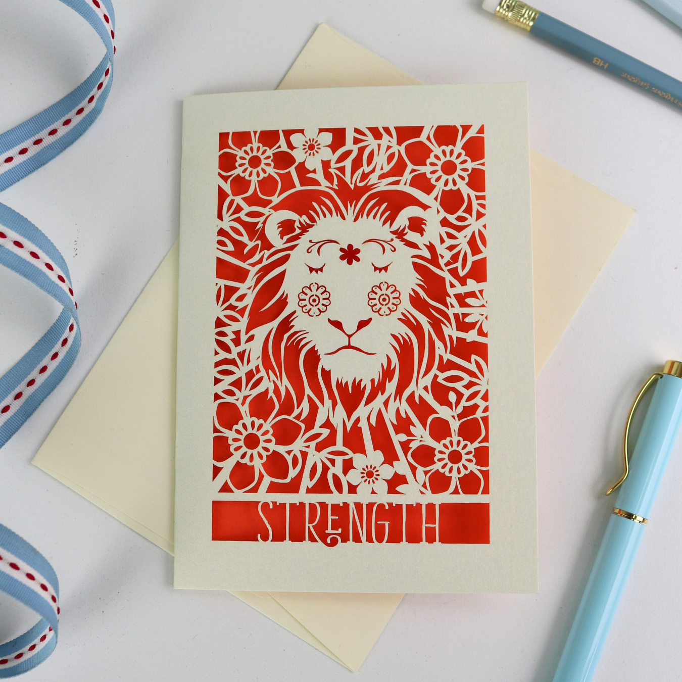 Card with a lion design and 'Strength' text on a white background with ribbons and a pen.