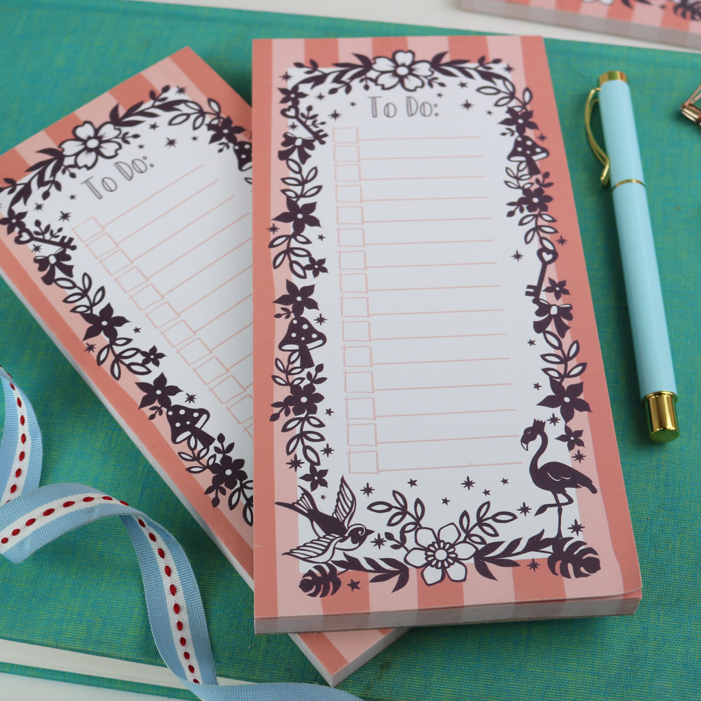 Two notepads on a turquoise surface, with a pen and ribbon