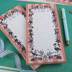 Two notepads on a turquoise surface, with a pen and ribbon