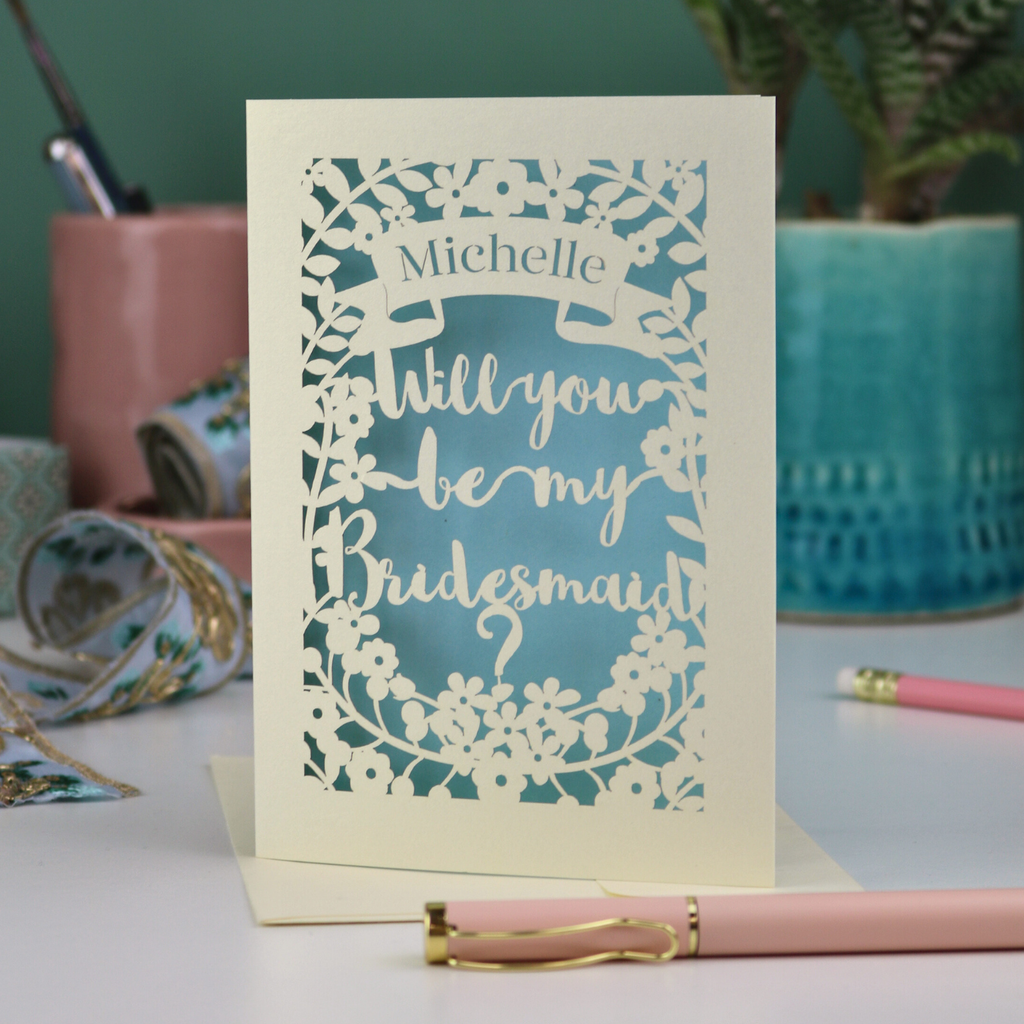 Bridesmaid proposal Card with 'Will you be my Bridesmaid?' text on a desk with stationery items.