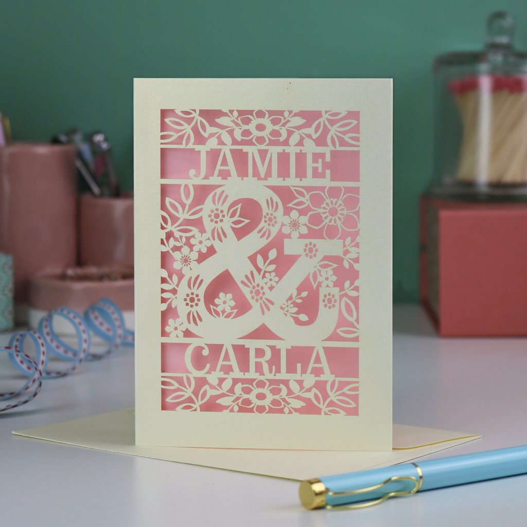 Personalised Engagement Card with laser-cut design of 'Jamie & Carla' on a table with stationery items.