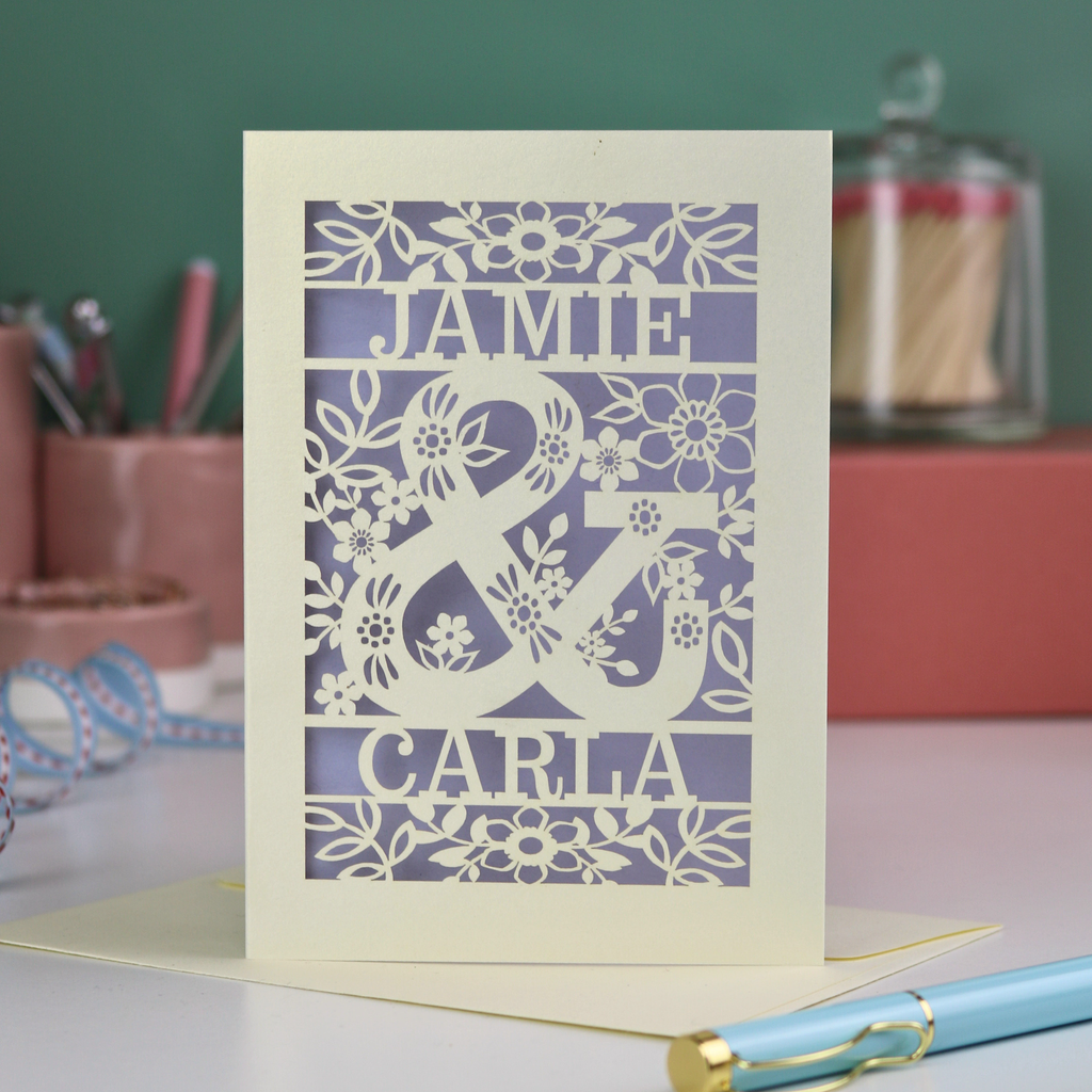 Personalised Engagement Card with laser-cut design of 'Jamie & Carla' on a table with stationery items.