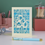 Personalised Engagement Card with laser-cut design of 'Jamie & Carla' on a table with stationery items.