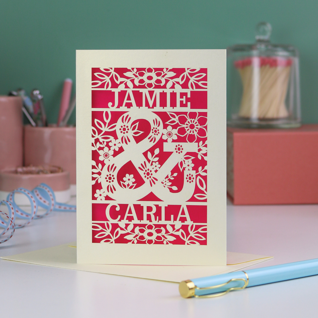 Personalised Engagement Card with laser-cut design of 'Jamie & Carla' on a table with stationery items.