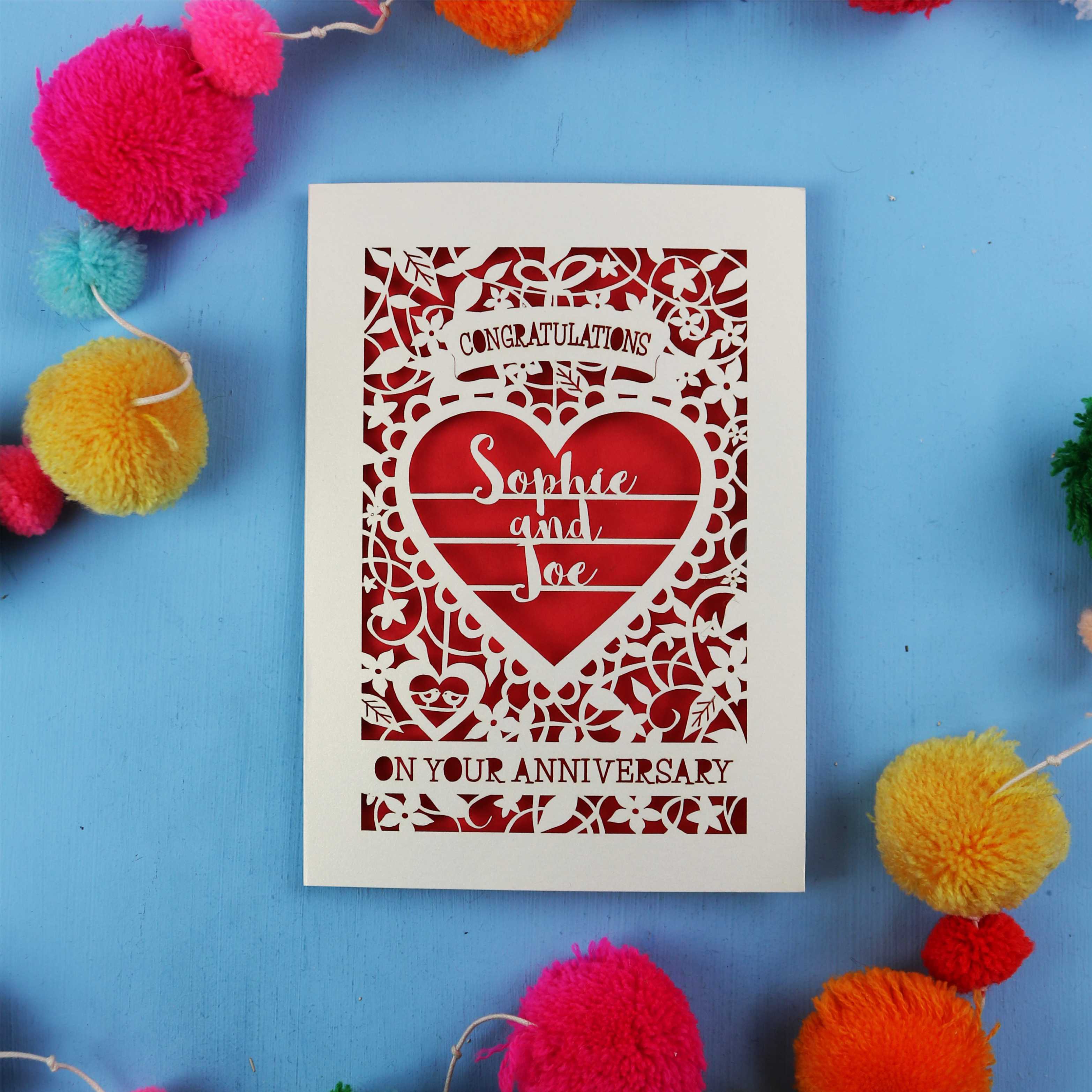 Personalised wedding anniversary card with decorative heart design on a blue background with colourful pom-poms.