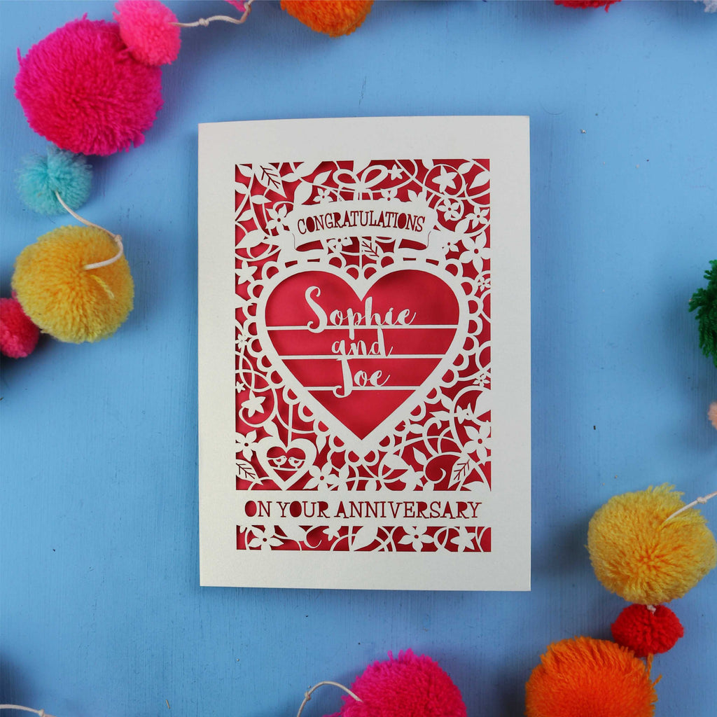 Cut out Anniversary card with red heart design on a blue background with colourful pom-poms