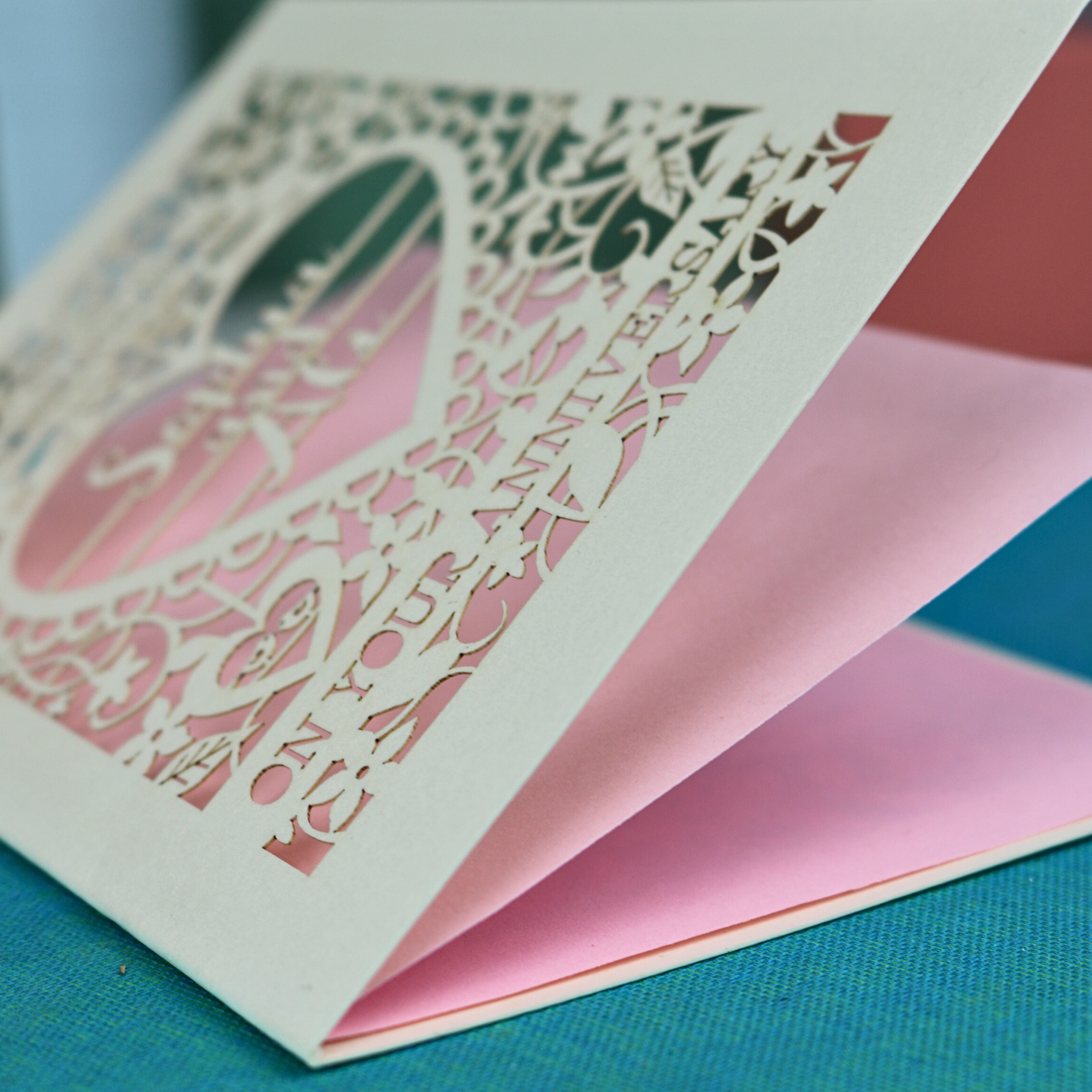 Laser-cut card with decorative text on a pink card against a blue background