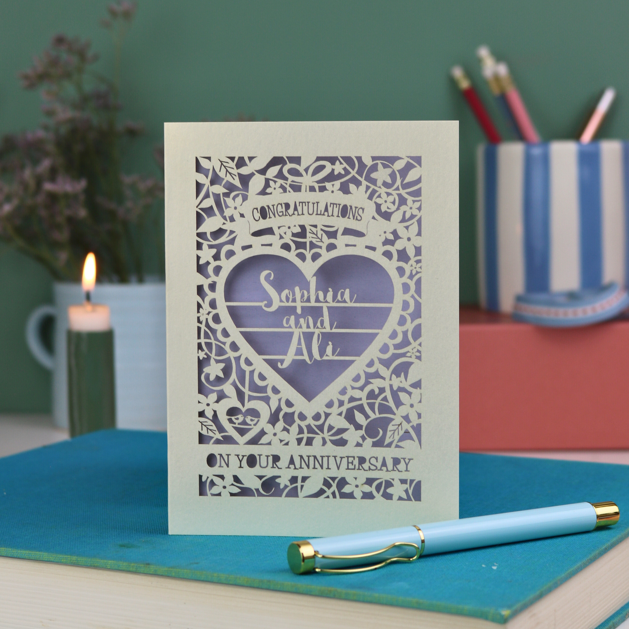 Anniversary card with decorative heart design on a table with a pen and candle.