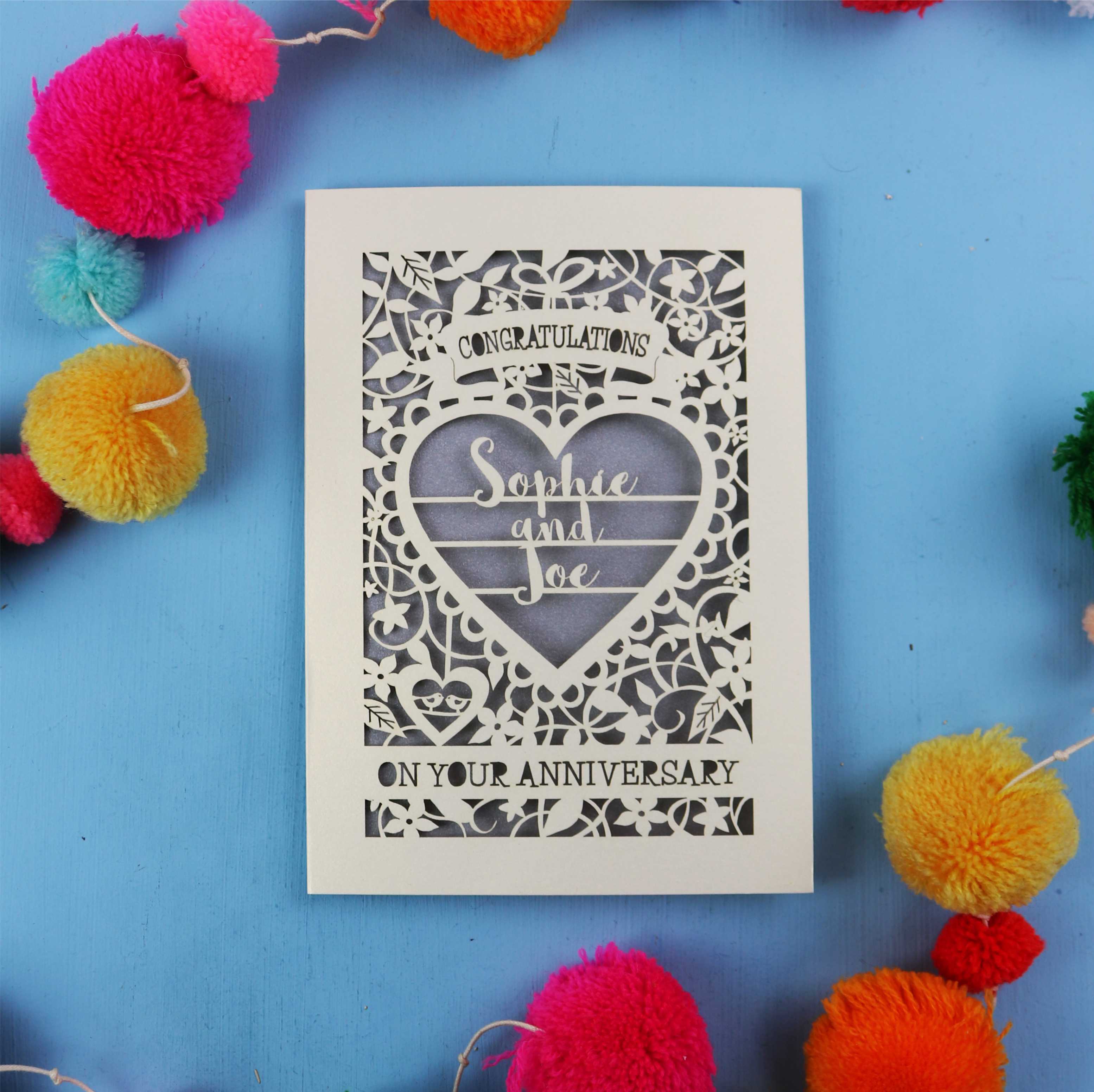 Laser cut Personalised wedding anniversary card with decorative heart design on a blue background with colourful pom-poms.