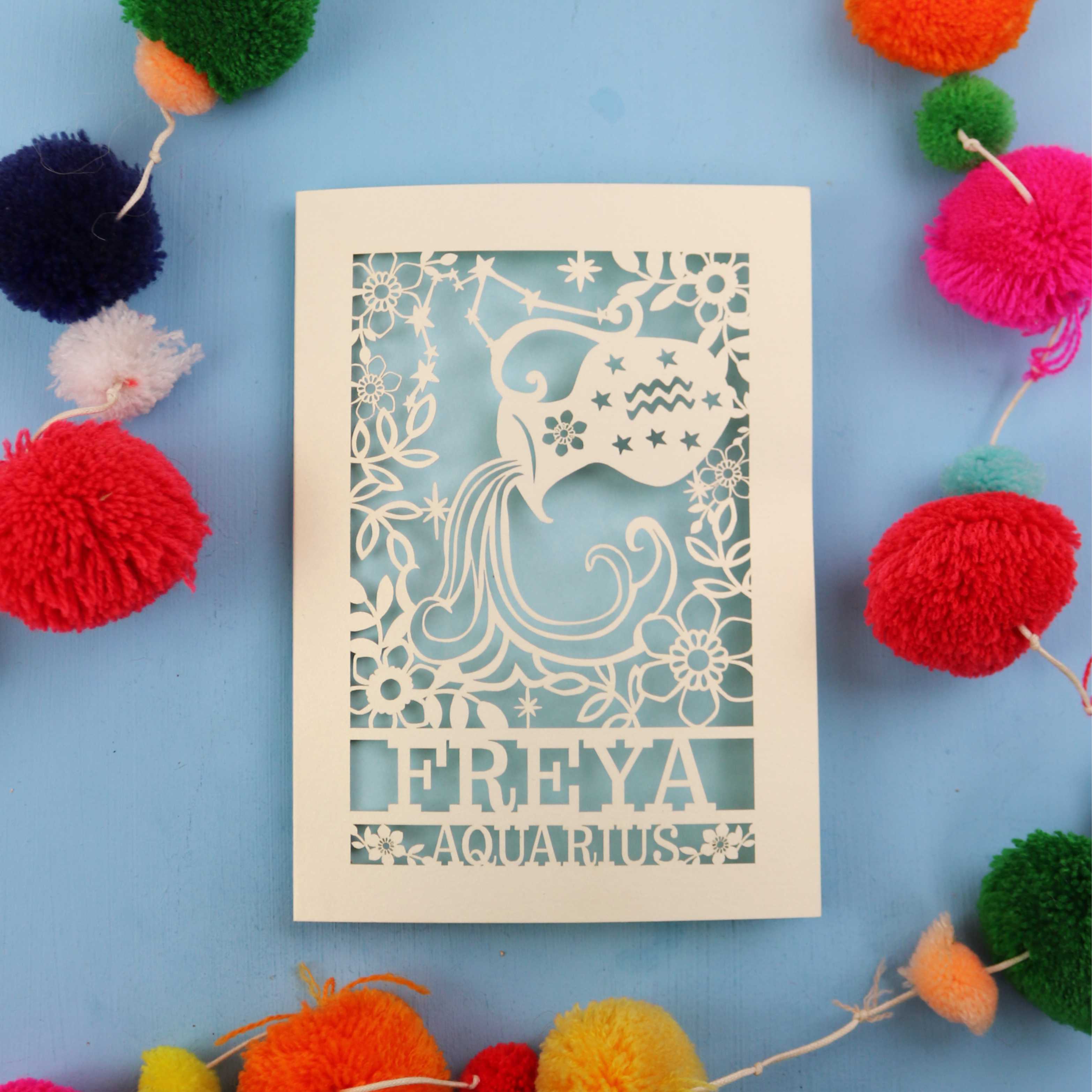 Decorative Aquarius Birthday card with 'FREYA AQUARIUS' design on a blue background with colourful pom-poms.
