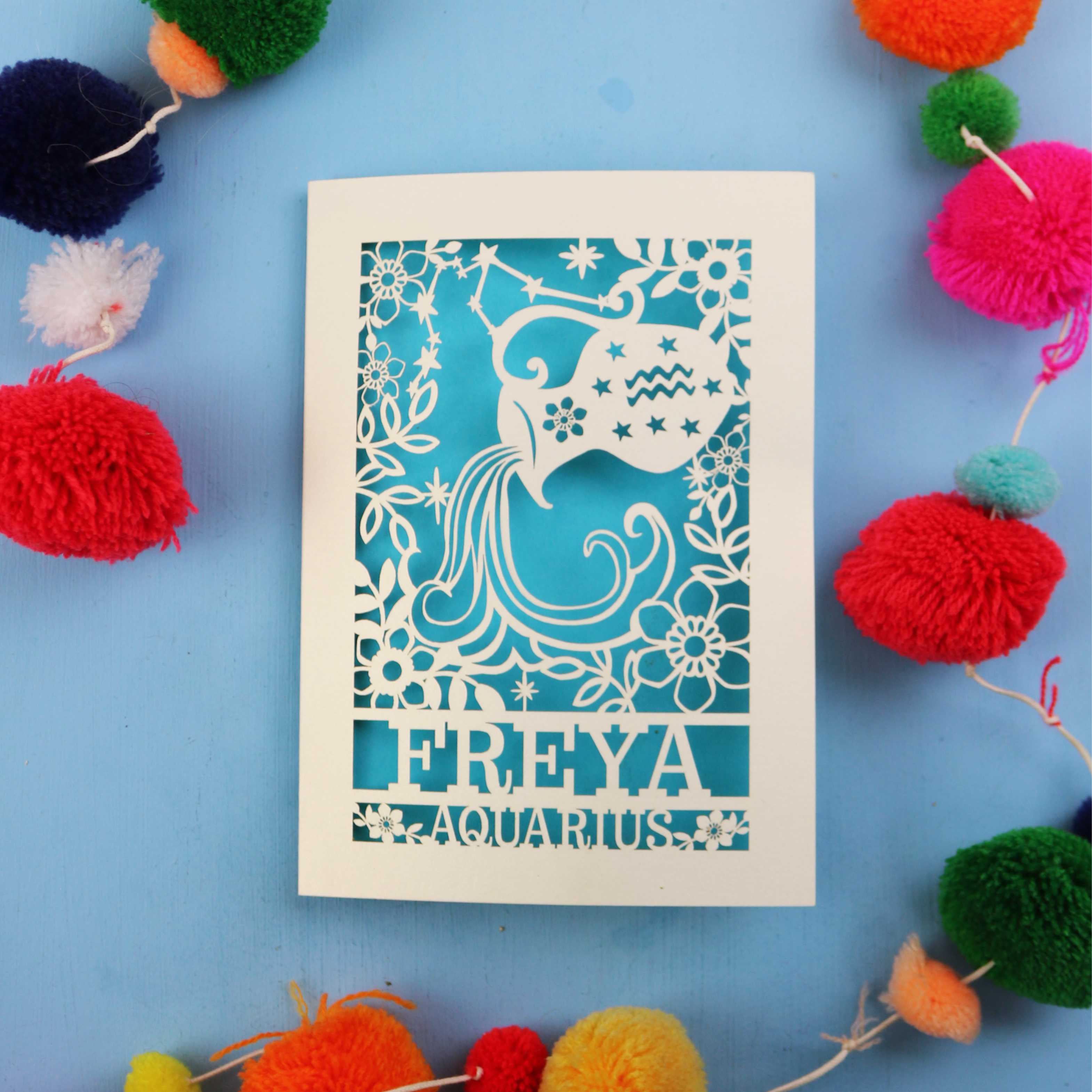 Decorative Aquarius Birthday card with 'FREYA AQUARIUS' design on a blue background with colourful pom-poms.