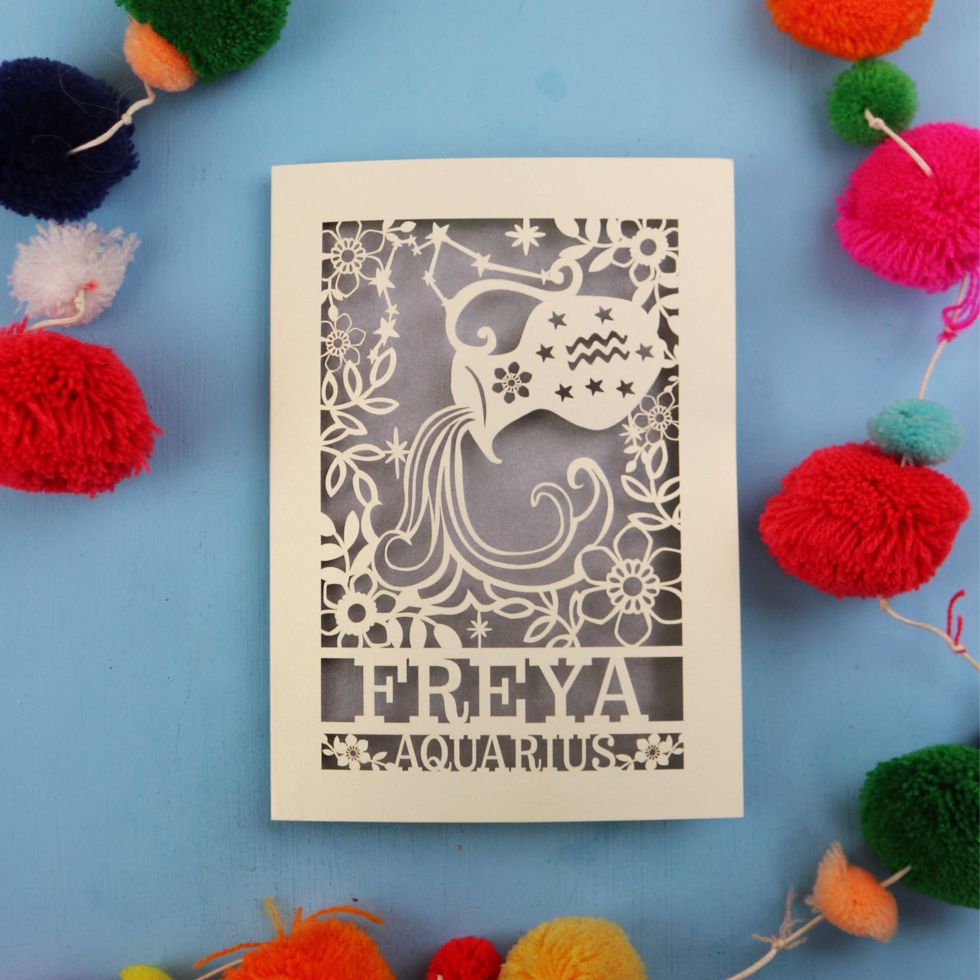 Decorative Aquarius Birthday card with 'FREYA AQUARIUS' design on a blue background with colourful pom-poms.