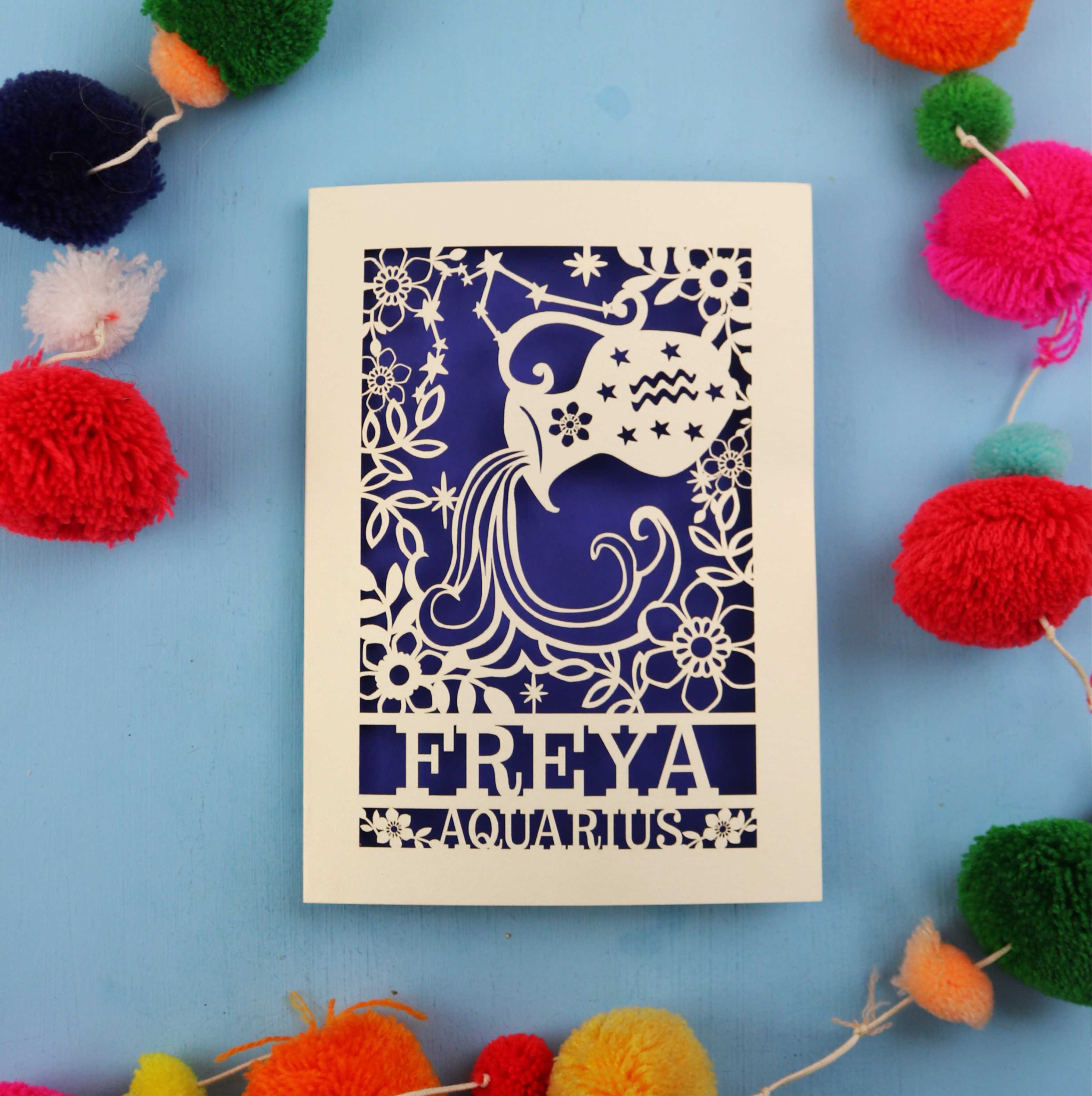 Decorative Aquarius Birthday card with 'FREYA AQUARIUS' design on a blue background with colourful pom-poms.
