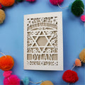 Laser-cut Bar Mitzvah card with Star of David and floral patterns on a blue background with colourful pom-poms.