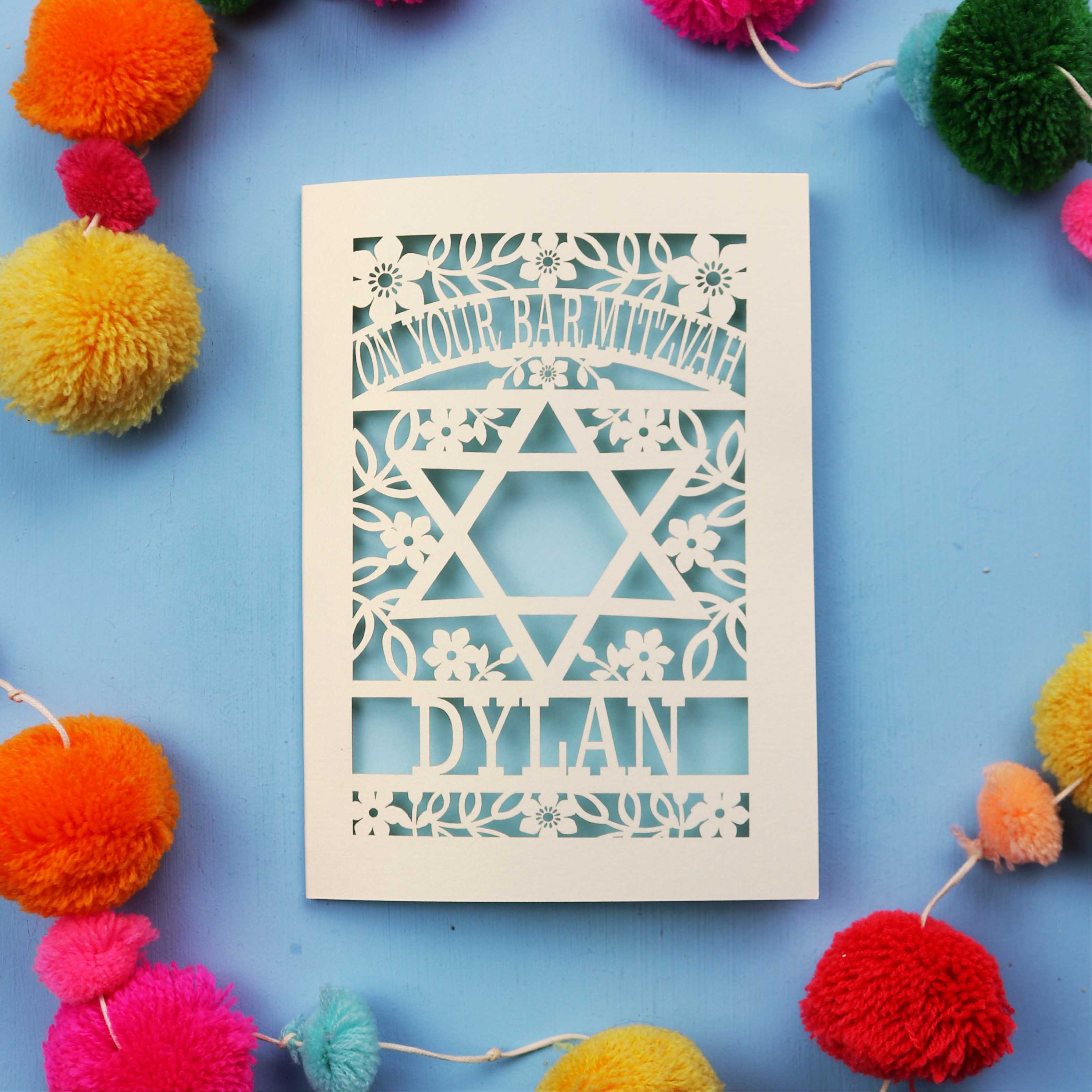 Personalised Bar Mitzvah Card with Star of David design and name 'Dylan' on a blue background with colourful pom-poms.