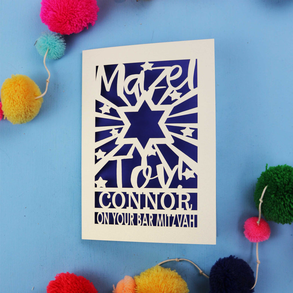 Bar Mitzvah Card with cut-out design and text on a blue background with colourful pom-poms.
