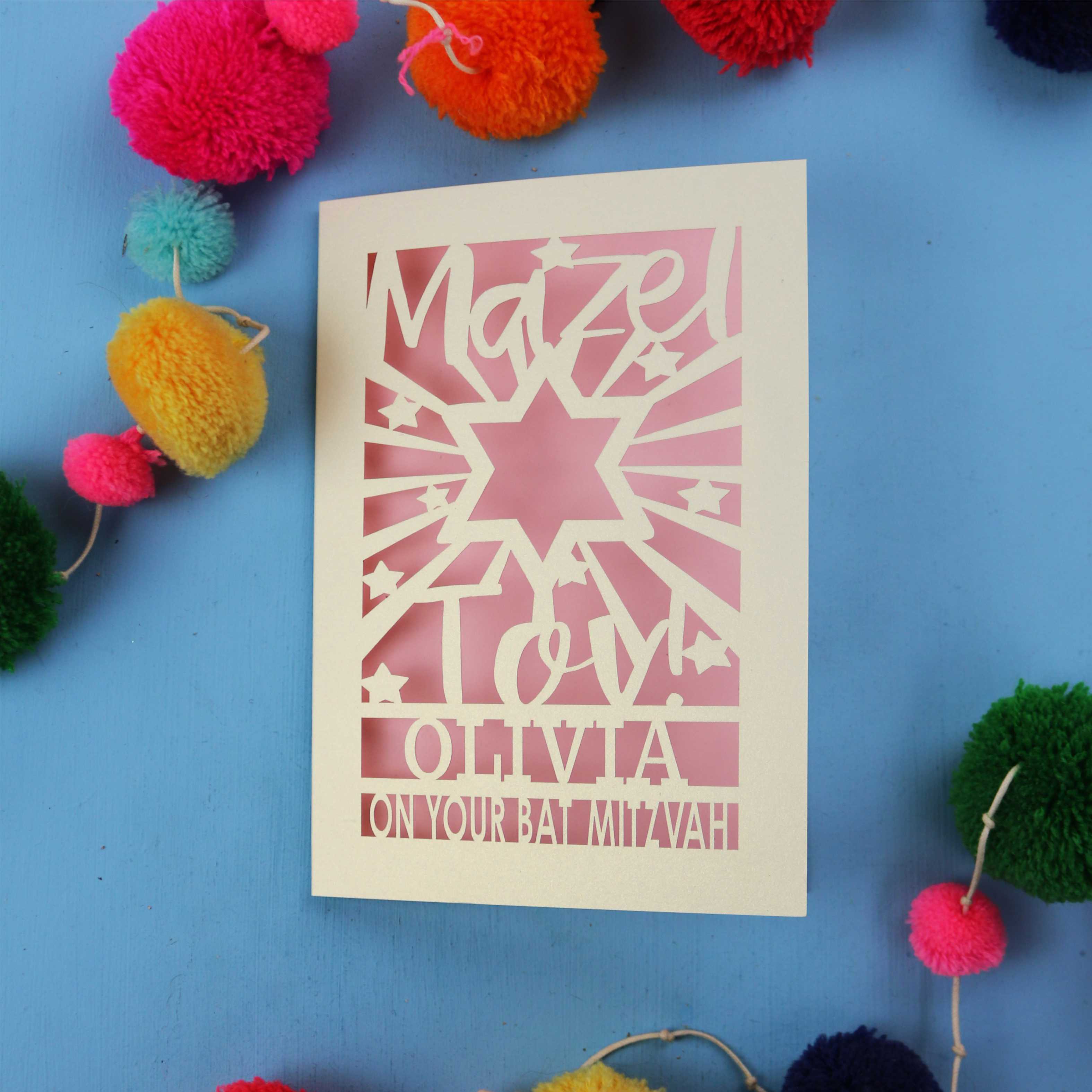 Personalized paper cut out Bat Mitzvah card with text on a blue background with colourful pom-poms.