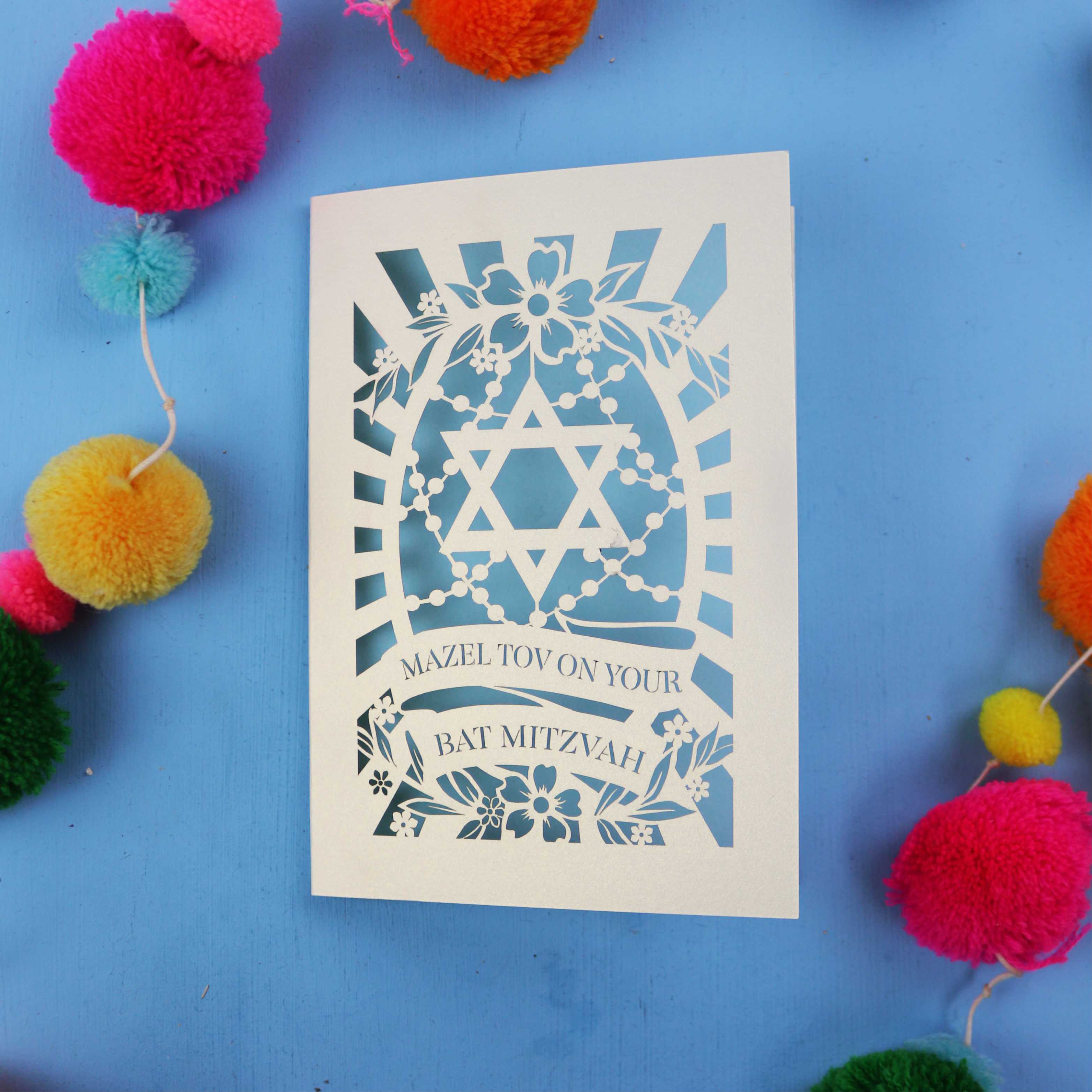 BatMitzvah card with Star of David design on a blue background with colourful pom-poms.