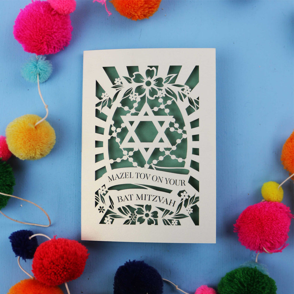 Laser cut Bat Mitzvah card with Star of David design on a blue background with colourful pom-poms.