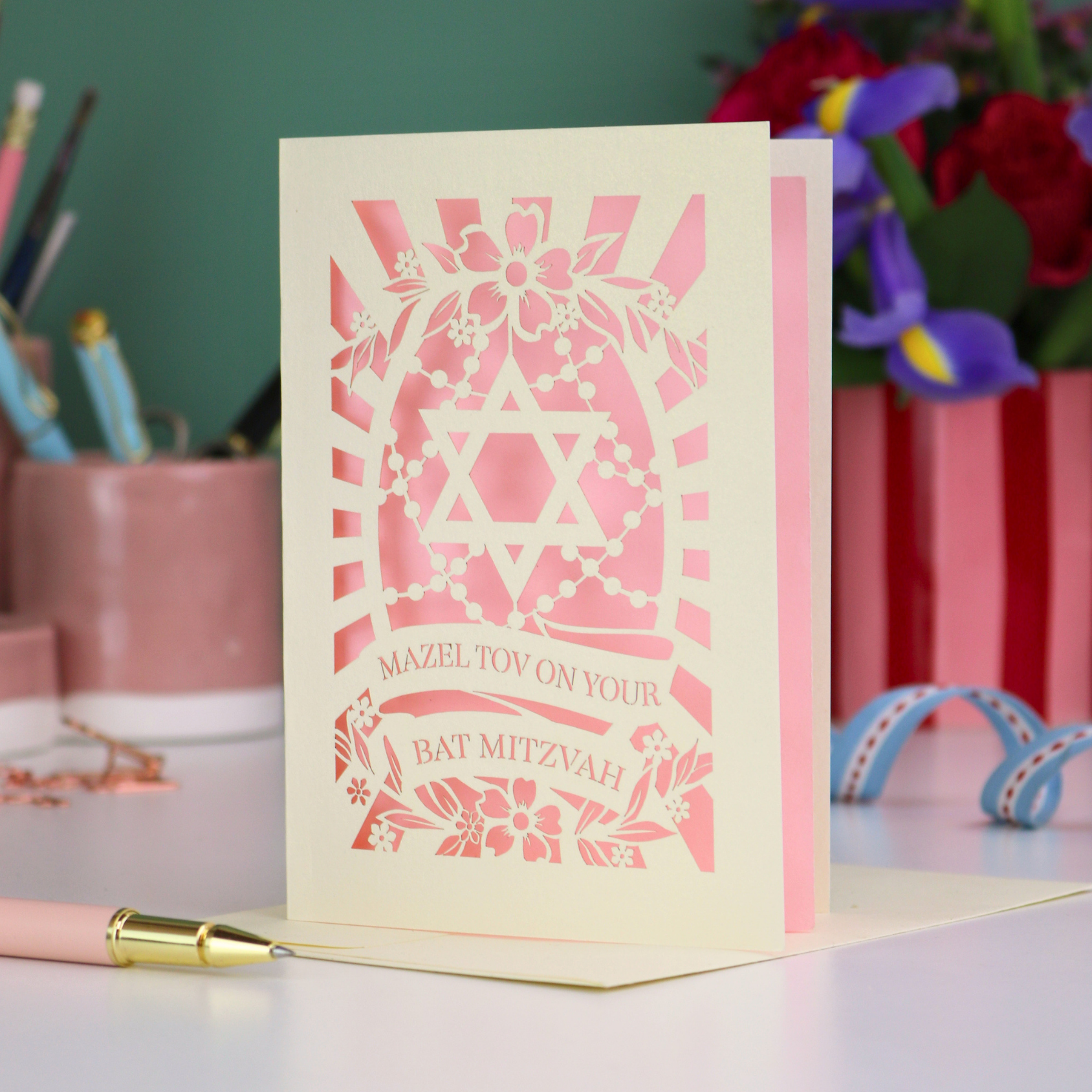 Pink Bat Mitzvah card with Star of David design on a desk with stationery items.