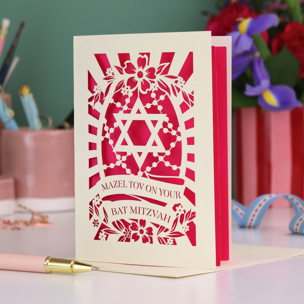 Bat Mitzvah card with Star of David design on a table with flowers and stationery.