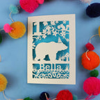 1st birthday Card with bear design and 'Bella' text on a blue background with colourful pom-poms.