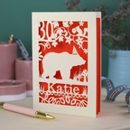 A laser cut birthday card personalised with an age and name, and featuring a cut out bear in a party hat with woodland border.
