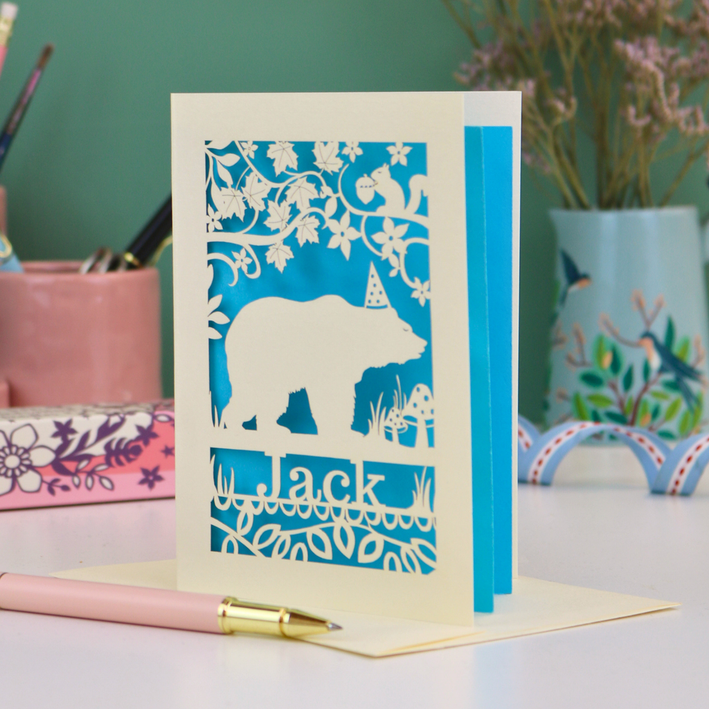 Husband birthday card with laser cut bear design and 'Jack' text on a table with stationery items.