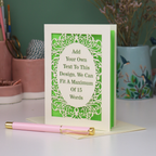 A custom laser cut personalised greeting card with a cream ornate filigree border and a green backing, displayed on a white surface with a pink pen in the foreground. The card features placeholder text that reads 'Add Your Own Text To This Design.