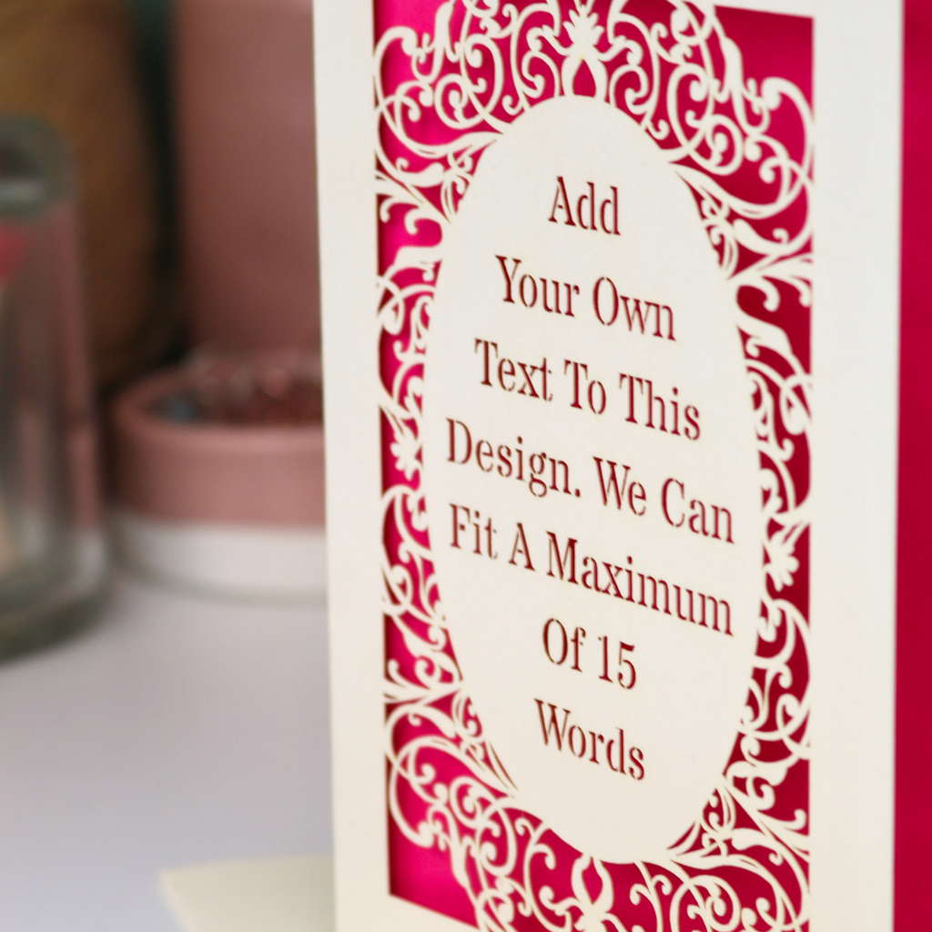 A close-up of a customizable greeting card or sign with a white central oval and pink ornate scrollwork border, containing placeholder text that says 'Add Your Own Text To This Design. We Can Fit A Maximum Of 15 Words.