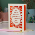 A bespoke cut out personalised greeting card with a cream ornate filigree border and orange backing, displayed on a white surface with a pink pen in the foreground. The card features placeholder text that reads 'Add Your Own Text To This Design.