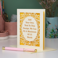 A bespoke laser cut personalised greeting card with a cream ornate filigree border and a yellow backing, displayed on a white surface with a pink pen in the foreground. The card features placeholder text that reads 'Add Your Own Text To This Design.