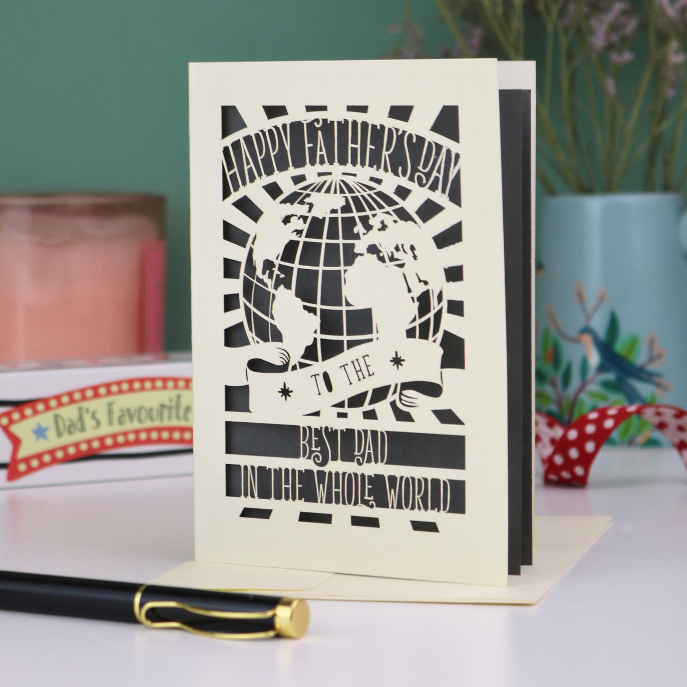 A cut out Father's Day card with globe design and the text "Happy Father's Day to the Best Dad In the Whole world", on a desk with pen and stationery items