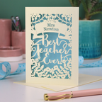 A cream laser cut card with floral design and the text "Mrs Newton. Best Teacher Ever!" Card has a light blue paper insert
