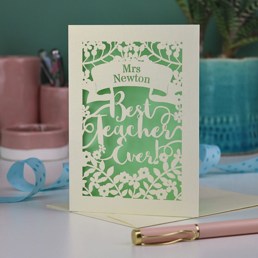 A cream laser cut card with floral design and the text "Mrs Newton. Best Teacher Ever!" Card has a light green paper insert