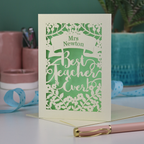 A cream laser cut card with floral design and the text "Mrs Newton. Best Teacher Ever!" Card has a light green paper insert