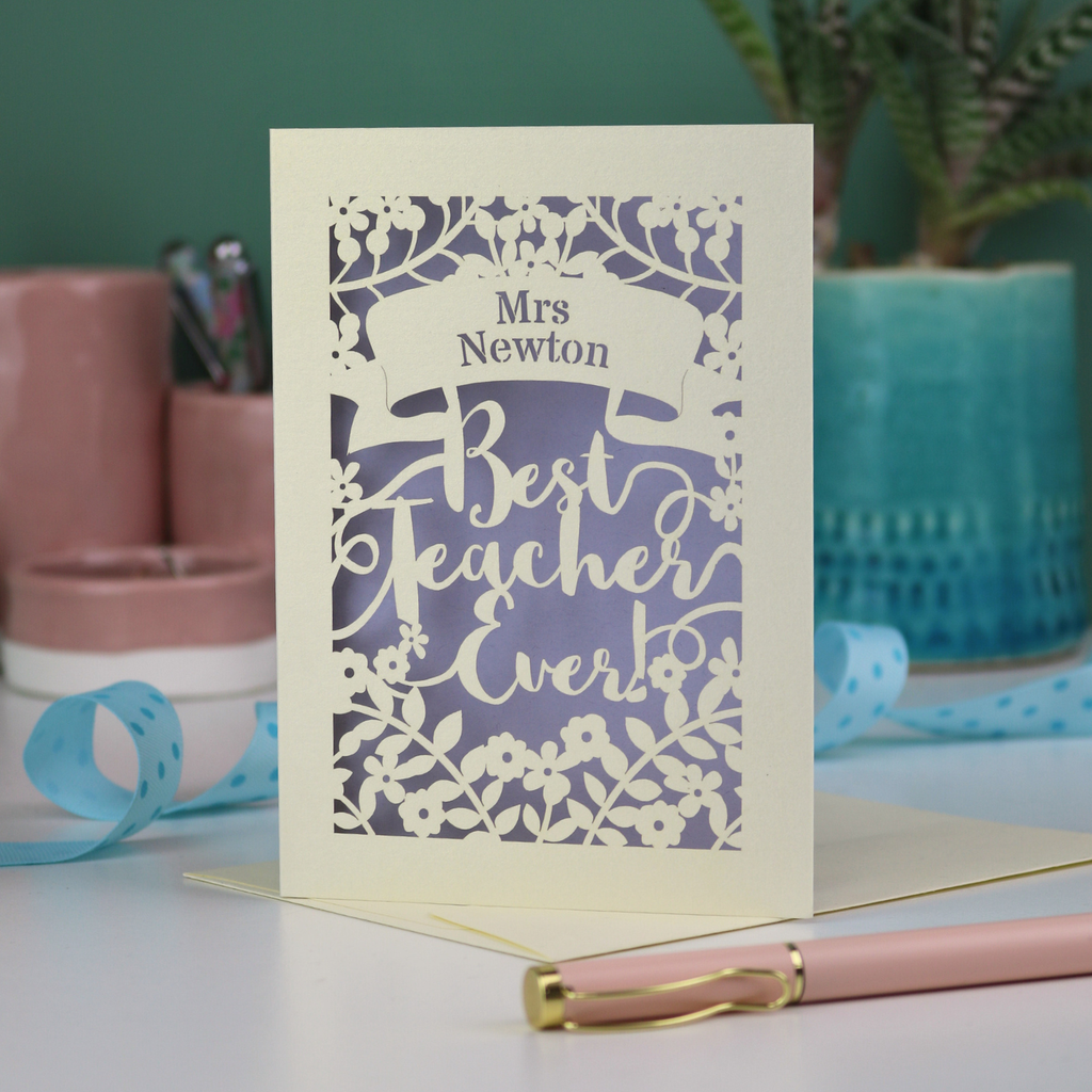 A cream laser cut card with floral design and the text "Mrs Newton. Best Teacher Ever!" Card has a lilac paper insert