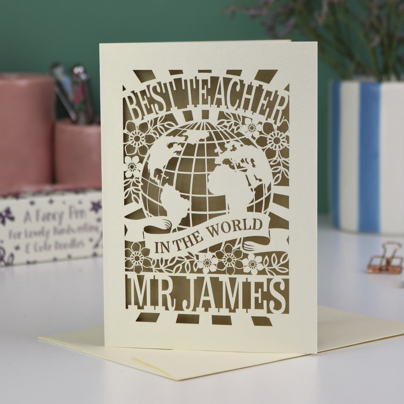 A laser cut cream and gold leaf thank you teacher card with globe design and the text Best Teacher in the World Mr James"