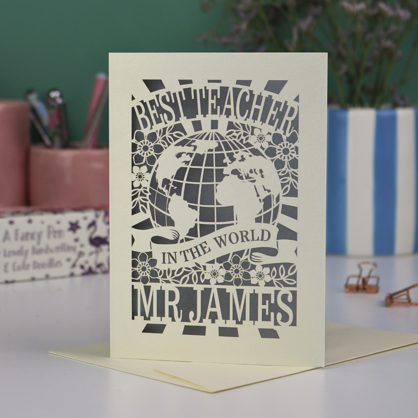 A laser cut cream thank you teacher card with globe design and the text Best Teacher in the World Mr James"